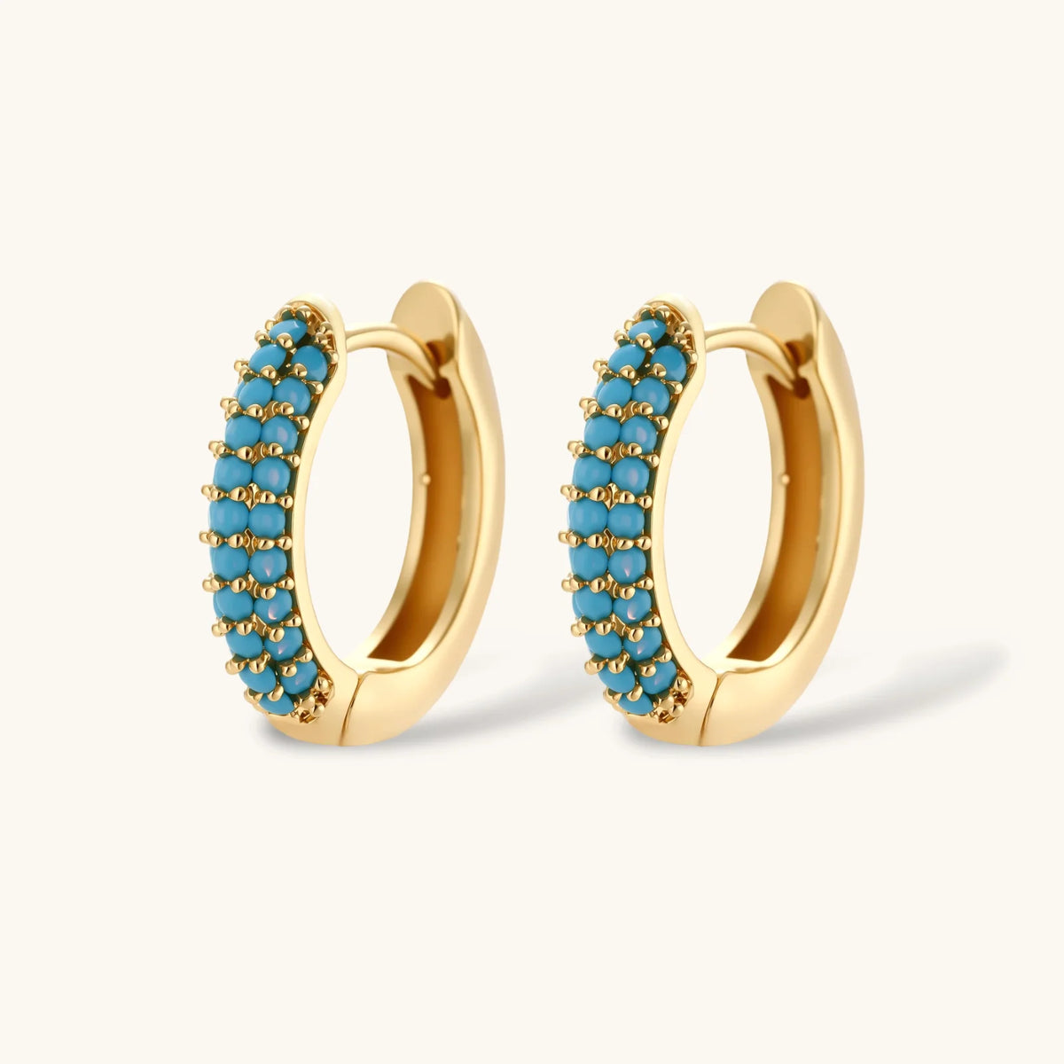 Gold-plated curved necklace and hoop earrings with turquoise cubic zirconia stones on white background.